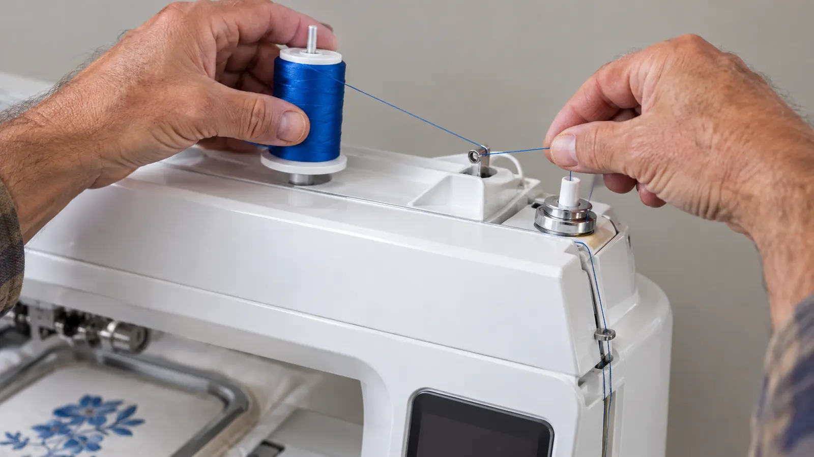 Close view of hands placing a spool of embroidery thread on a home machine and guiding the thread through the top path