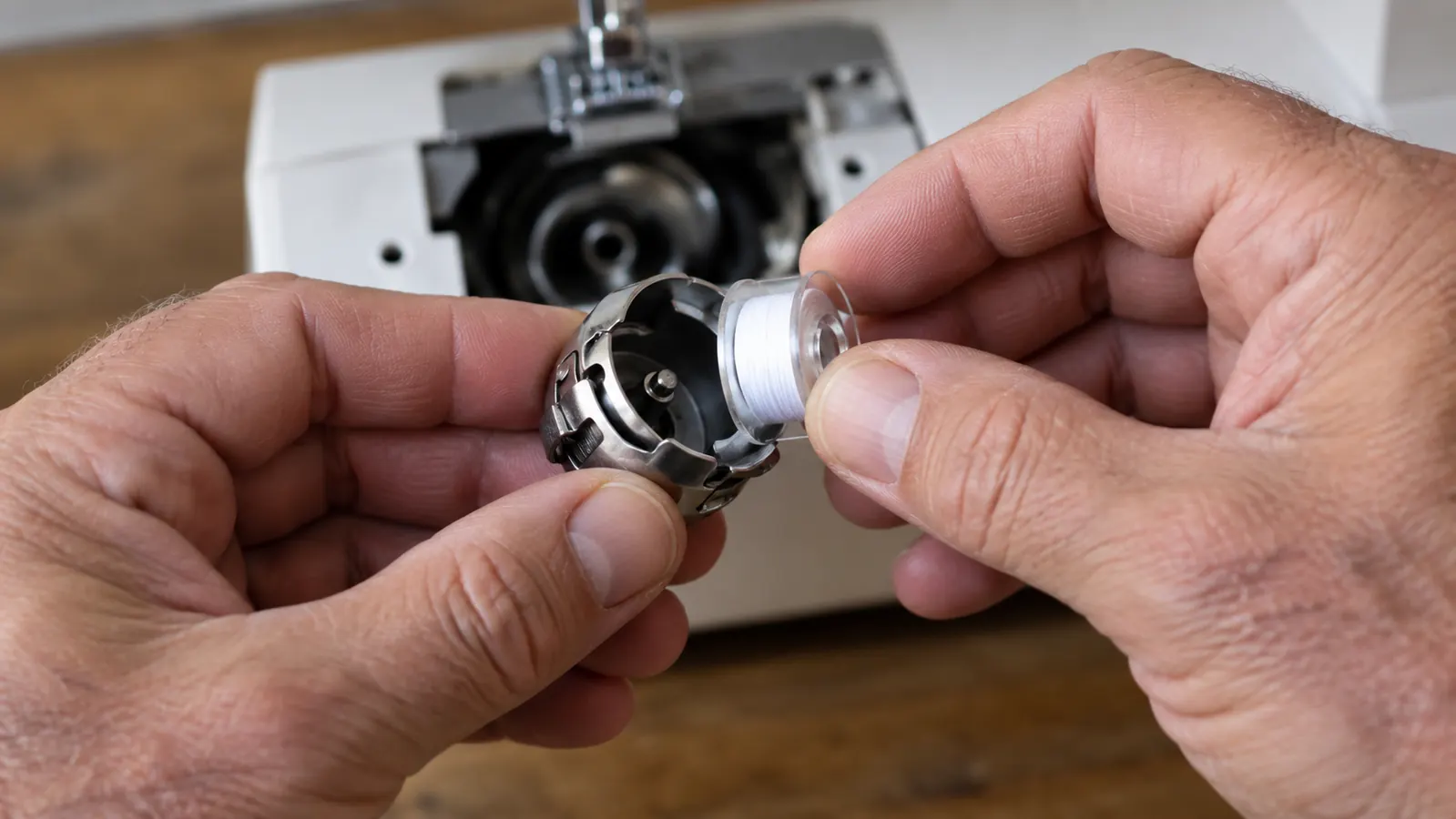 Hands loading a prewound bobbin into the bobbin case of an embroidery machine